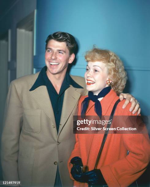 Ronald Reagan , wearing a beige jacket with dark blue shirt with a wide collar, and his wife, Jane Wyman , US actress, wearing a red coat with a dark...