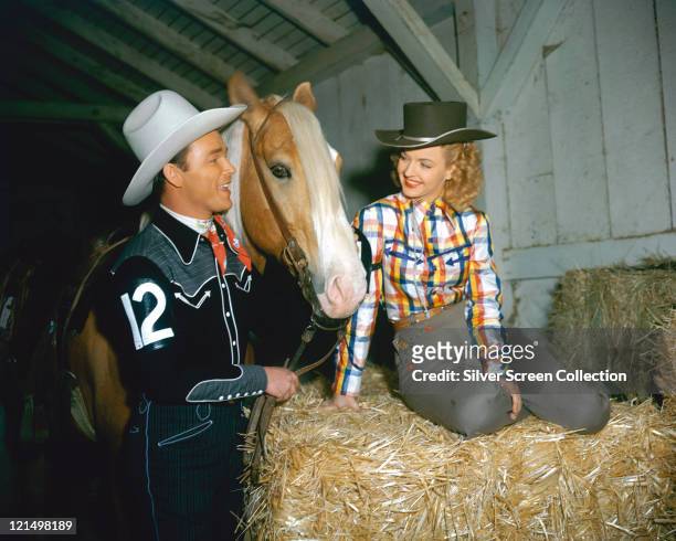 Roy Rogers , US actor and singer, wearing a white cowboy hat, red neckerchief and western shirt, posing beside his palomino horse, Trigger , and his...