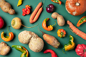 Trendy ugly organic vegetables. Assortment of fresh eggplant, onion, carrot, zucchini, potatoes, pumpkin, pepper in craft paper bag over green background. Top view. Cooking ugly food concept. Non gmo vegetables