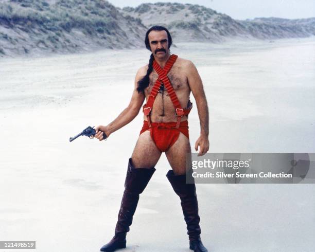 Sean Connery, British actor, holding a handgun while wearing thigh-high boots and red costume, with his hair in a pony tail, standing in a snowy...