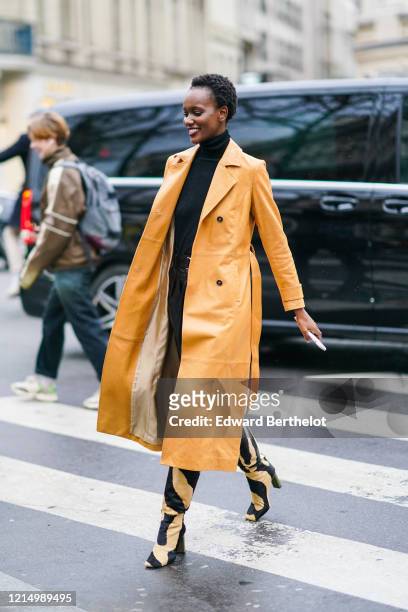 Model wears an orange long trench coat, a black turtleneck pullover, beige and black zebra print pattern pointy boots, outside Ralph & Russo, during...