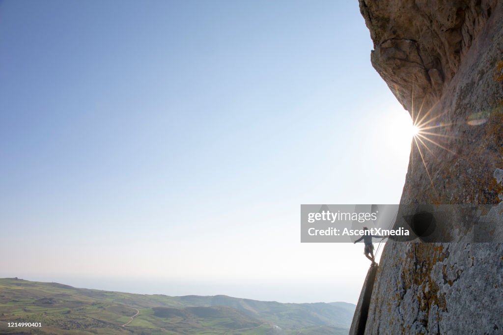 Mountain climber ascends rock face at sunrise