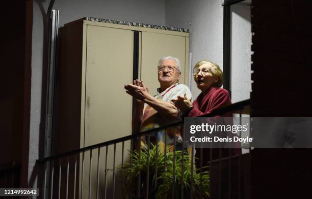 An elderly couple applaud from their balcony to acknowledge the battle being fought by doctors, nurses and hospital staff across the country on March...