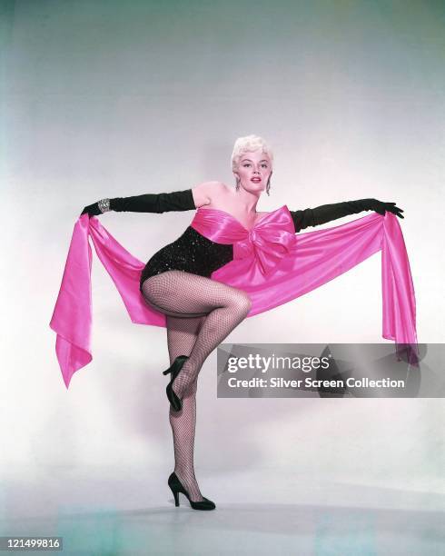 Sheree North , US actress, singer and dancer, wearing a black leotard with fishnet stockings and long black gloves, holding a length of pink fabric...