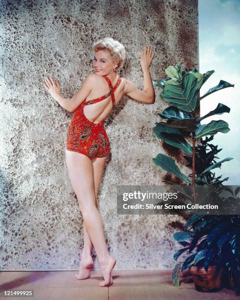 Sheree North , US actress, singer and dancer, looking over her shoulder as she poses, wearing a cross-back print pattern red swimsuit, posing against...