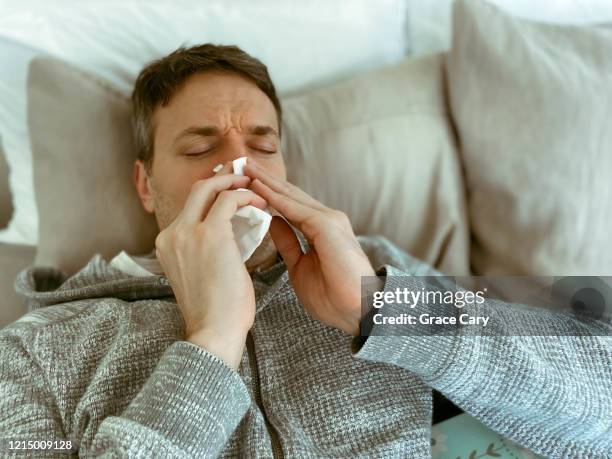 sick man sneezes in bed - symptom stockfoto's en -beelden