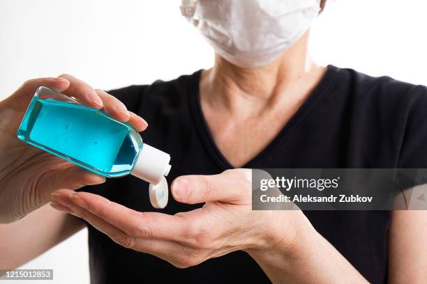 an elderly woman in a medical disposable mask disinfects her hands with an antiseptic alcohol gel. - hand holding a bottle stock pictures, royalty-free photos & images