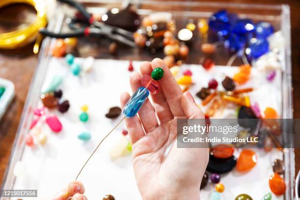 female model makes jewelry using beads, pliers and other tools at a workbench - jewelry making stock pictures, royalty-free photos & images