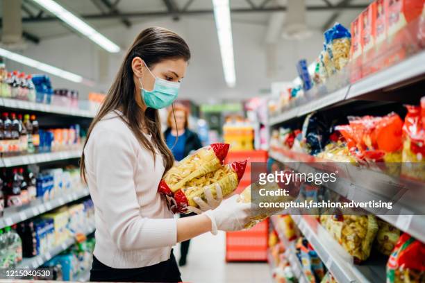 buyer wearing a protective mask.shopping during the pandemic quarantine.nonperishable smart purchased household pantry groceries preparation.woman buying few pasta packages.budget pastas and noodles. - covid 19 food stock pictures, royalty-free photos & images