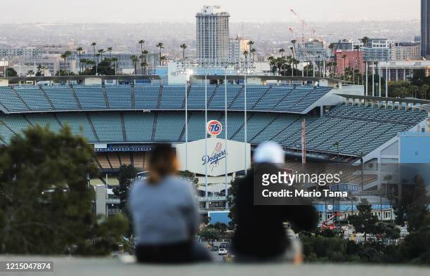 People sit on a hill overlooking Dodger Stadium on what was supposed to be Major League Baseball's opening day, now postponed due to the coronavirus,...