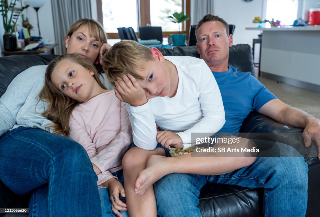 Coronavirus lockdow. Familia aburrida viendo la televisión indefensa en aislamiento en casa durante la cuarentena COVID 19 Brote. Los bloqueos obligatorios y las recomendaciones de autoaislamiento obligan a las familias a permanecer en casa.