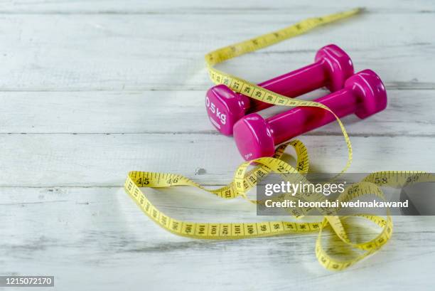 pink dumbbell with yellow measuring tape on white wood background - fat loss stock-fotos und bilder