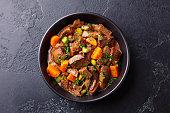 Beef meat and vegetables stew in black bowl. Slate background. Top view.
