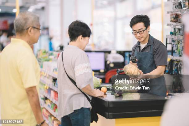 an asian chinese senior adult queuing to pay for her shopping items to cashier at counter check out in supermarket - supermarket queue stock pictures, royalty-free photos & images
