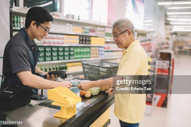 een aziatische chinese hogere volwassene die voor zijn het winkelen punten aan kassier bij telleruitcheckt in supermarkt betaalt - bank counter old stockfoto's en -beelden