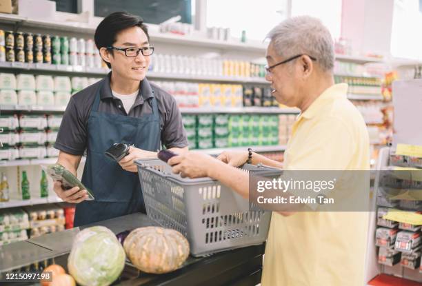 an asian chinese senior adult paying for his shopping items to cashier at counter check out in supermarket - checkout conveyor belt stock pictures, royalty-free photos & images