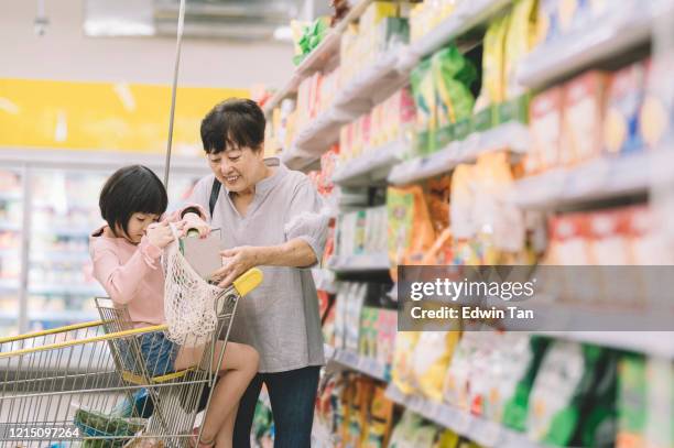 an asian chinese senior woman and her granddaughter shopping at the grocery dairy product section for food - grandmother granddaughter stock pictures, royalty-free photos & images