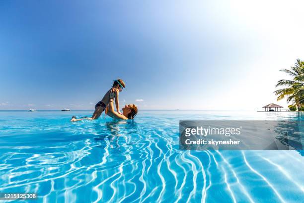 petit garçon heureux ayant l’amusement avec sa mère pendant la journée d’été dans la piscine. - piscine à débordement photos et images de collection