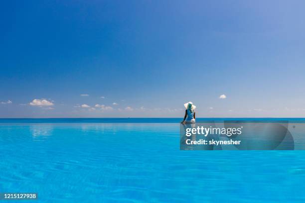vue arrière d’une femme regardant la vue de mer d’une piscine à débordement. - piscine à débordement photos et images de collection