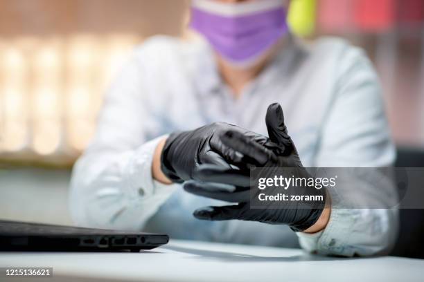 het zetten van zwarte beschermende handschoenen op handen alvorens laptop te gebruiken - zwarte handschoen stockfoto's en -beelden