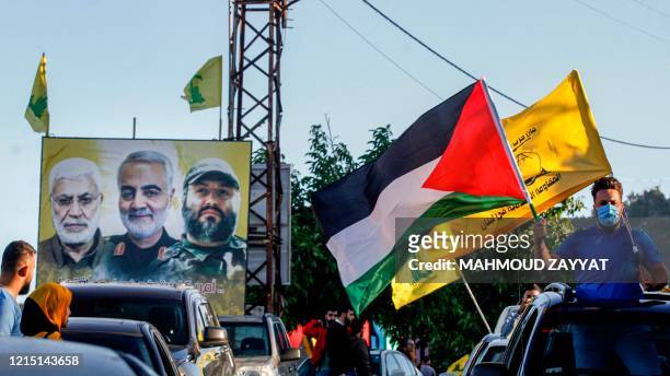 Supporter of the Lebanese Shiite movement Hezbollah waves Palestinian and Hezbollah flags while riding in a vehicle past a billboard showing the...