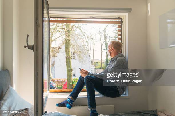 man with mask looking out of window - quarantine stock pictures, royalty-free photos & images