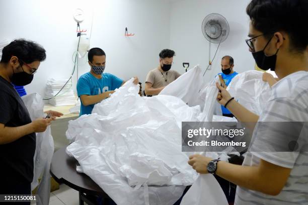 Workers wearing protective masks work together to pack protective suits at a production facility in Kuala Lumpur, Malaysia, on Thursday, May 21,...