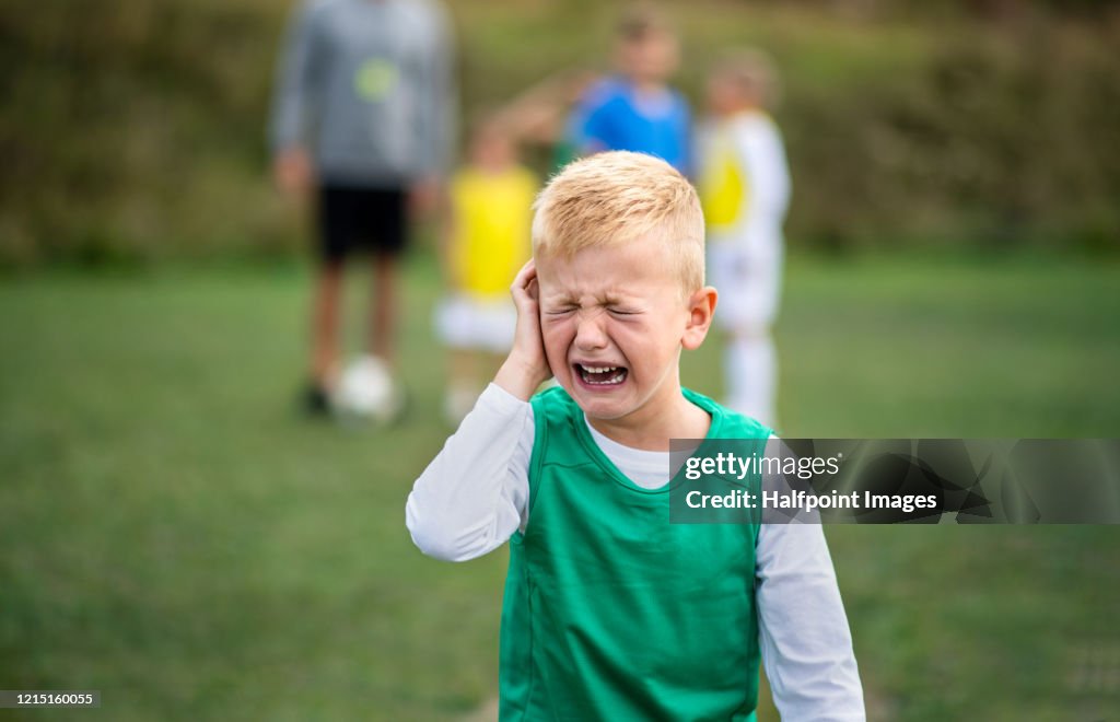 Small boy in pain crying outdoors on football pitch.
