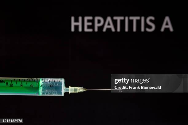 This photo illustration shows a disposable syringe with hypodermic needle, HEPATITIS A written on a black board behind.