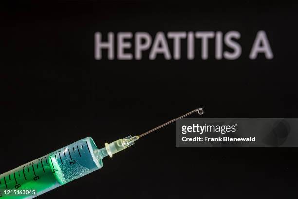 This photo illustration shows a disposable syringe with hypodermic needle, HEPATITIS A written on a black board behind.