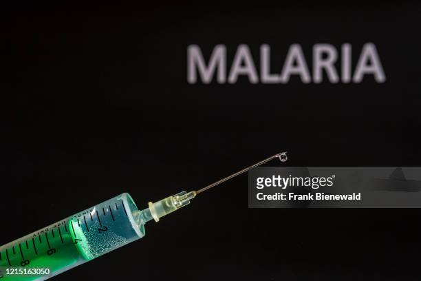 This photo illustration shows a disposable syringe with hypodermic needle, MALARIA written on a black board behind.