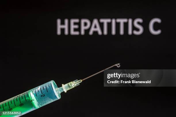 This photo illustration shows a disposable syringe with hypodermic needle, HEPATITIS C written on a black board behind.