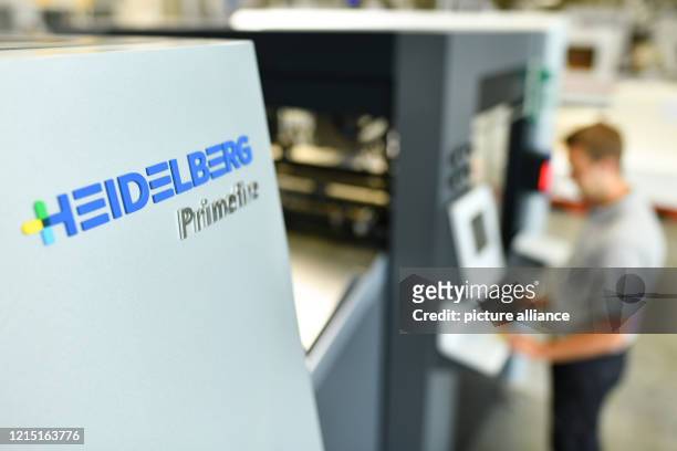 June 2018, Baden-Wuerttemberg, Wiesloch: An employee stands behind a company logo on a "Primefire 106" digital printing press at the Heidelberger...