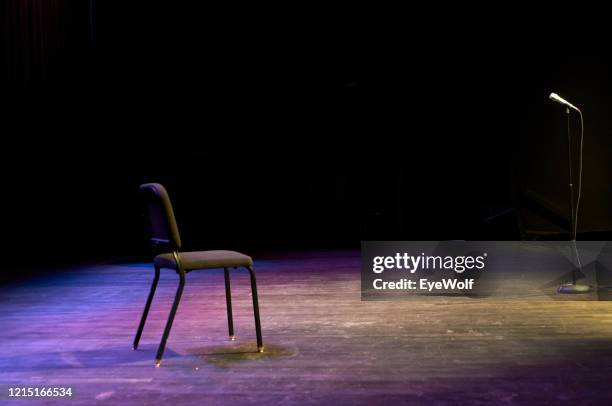 a chair and a microphone stand sitting on a stage with no people with dramatic lighting - microphone stand stock-fotos und bilder
