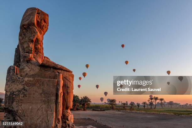 colossi of memnon at dawn with hot air balloons in the sky, luxor, nile valley, egypt - luxor stock-fotos und bilder