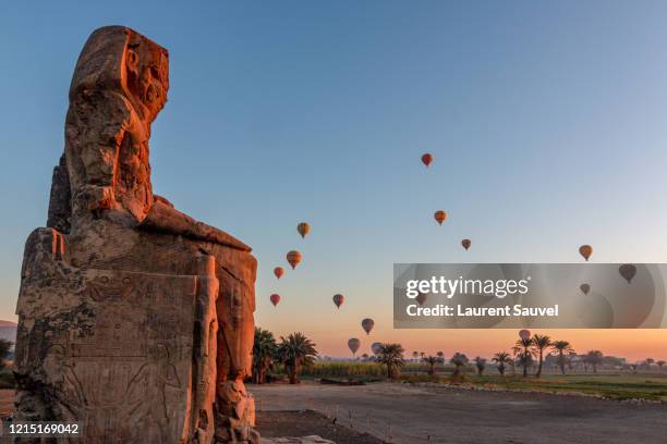 colossi of memnon at dawn with hot air balloons in the sky, luxor, nile valley, egypt - valle de los reyes fotografías e imágenes de stock