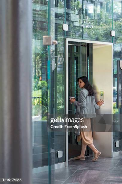 llegada al trabajo: una empresaria asiática entra en un ascensor en un edificio de oficinas - entrando fotografías e imágenes de stock