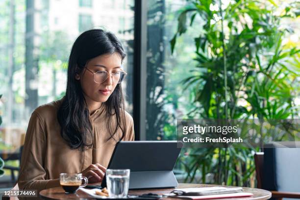 freelance business: asian businesswoman working on a tablet at a cafe - using digital tablet asian stock pictures, royalty-free photos & images