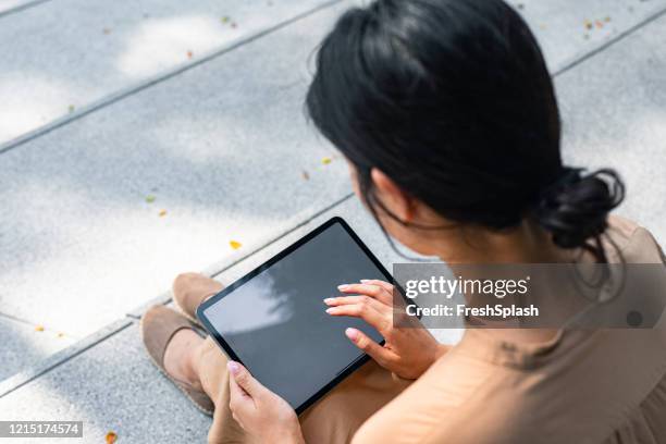 over the shoulder view of an asian woman sitting on stairs and using a digital tablet (copy space) - computer screen over shoulder stock pictures, royalty-free photos & images