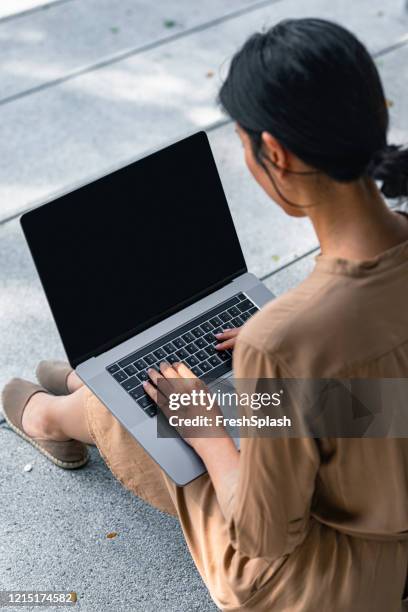 over the shoulder view of an asian woman sitting on stairs and working on her laptop computer (copy space) - computer screen over shoulder stock pictures, royalty-free photos & images