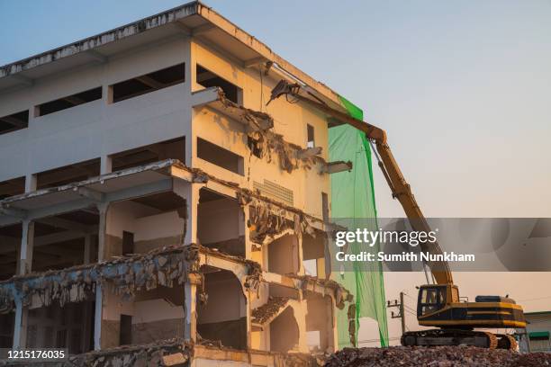 dismantling of an old factory by backhoe breaking concrete structure of industrial building in the construction site - collapsing wall stock pictures, royalty-free photos & images