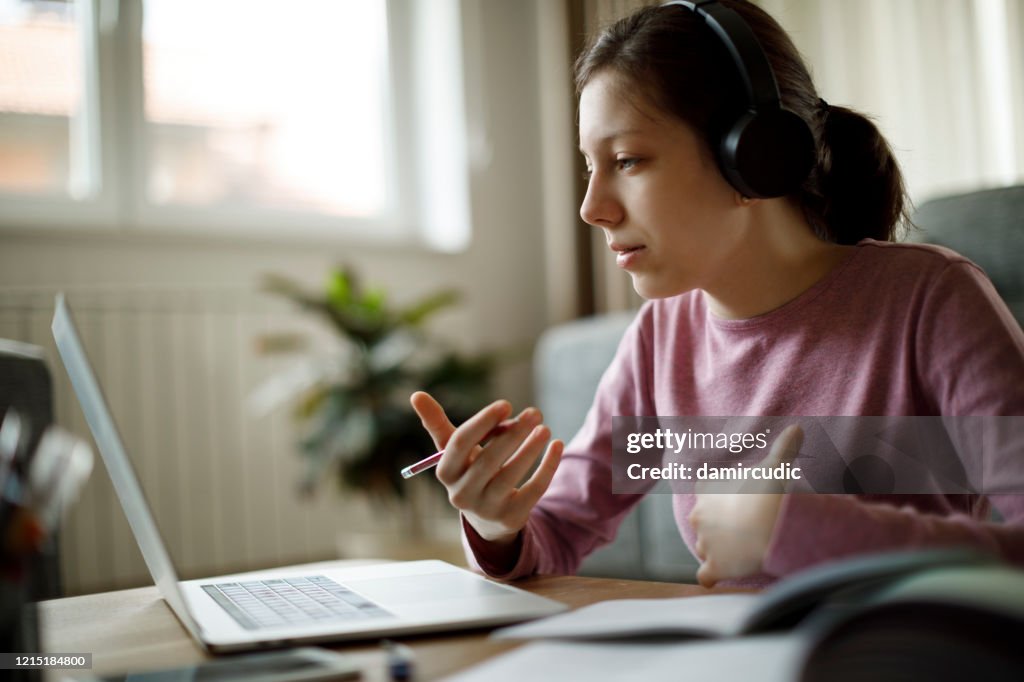 Teenage girl with headphones having online school class at home