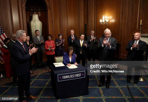 Speaker of the House Nancy Pelosi , surrounded by a bipartisan group of members of the House, signs the stimulus bill known as the CARES Act after...