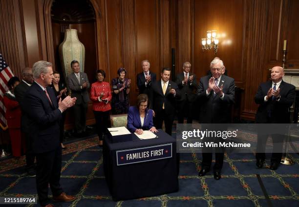 Speaker of the House Nancy Pelosi , surrounded by a bipartisan group of members of the House, signs the stimulus bill known as the CARES Act after...