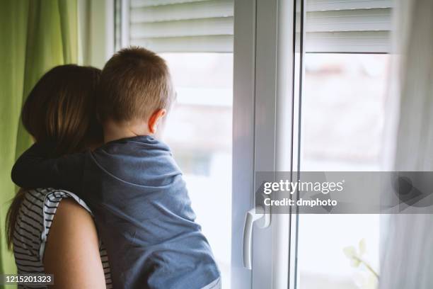 mom and son looking through window at home - boy hugs mother stock pictures, royalty-free photos & images