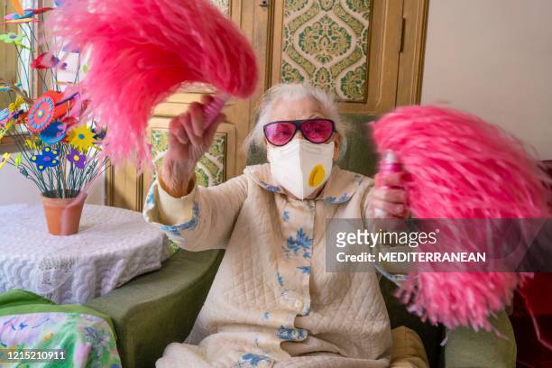 coronavirus covid-19 pandemic confinement with mask an humor cheerleader pom-pom elderly woman happy - white pom pom stock pictures, royalty-free photos & images