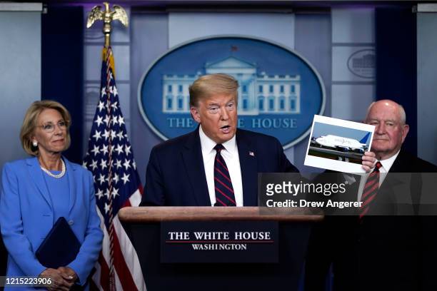 President Donald Trump holds up a picture of a Boeing 747 Dreamlifter as Secretary of Education Betsy DeVos and Secretary of Agriculture Sonny Perdue...