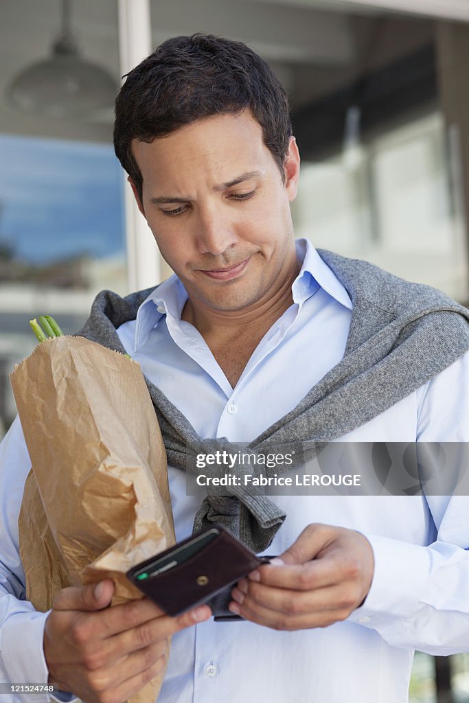 Mid adult man checking the empty wallet with paper bag full of vegetables