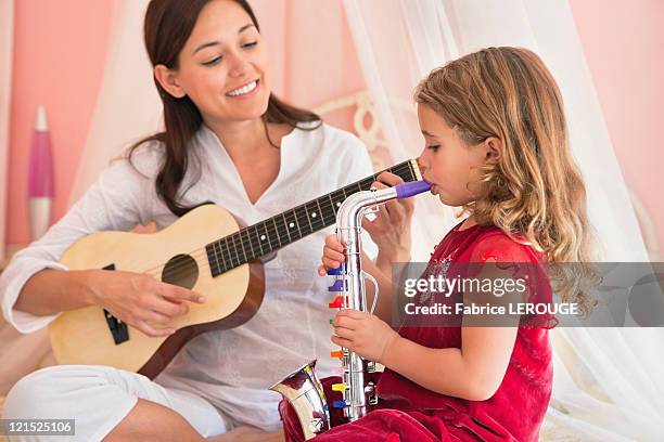 woman playing guitar with her daughter playing saxophone - sax stockfoto's en -beelden