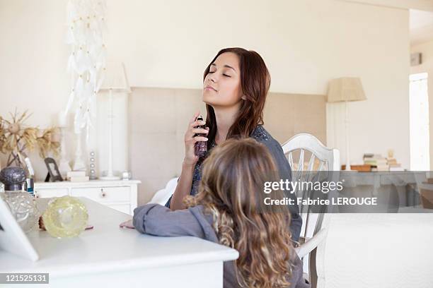 young woman applying perfume while her daughter beside her - tocador fotografías e imágenes de stock